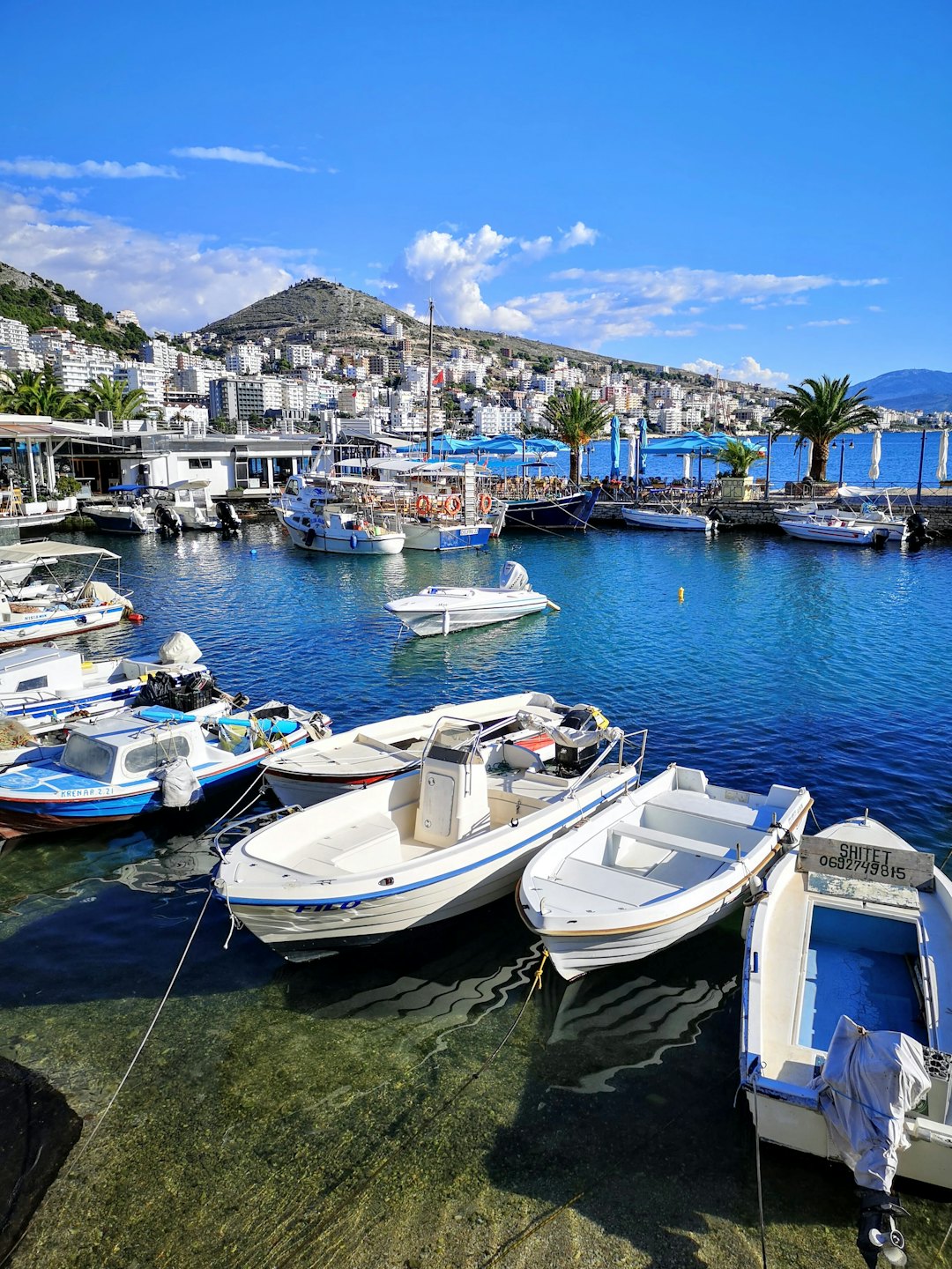Piccole barche ormeggiate in un porto turistico mediterraneo accanto a un paese collinare.