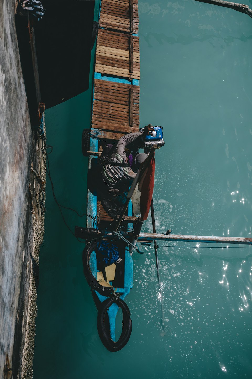 Un uomo ripara un motore fuoribordo su una barca di legno.
